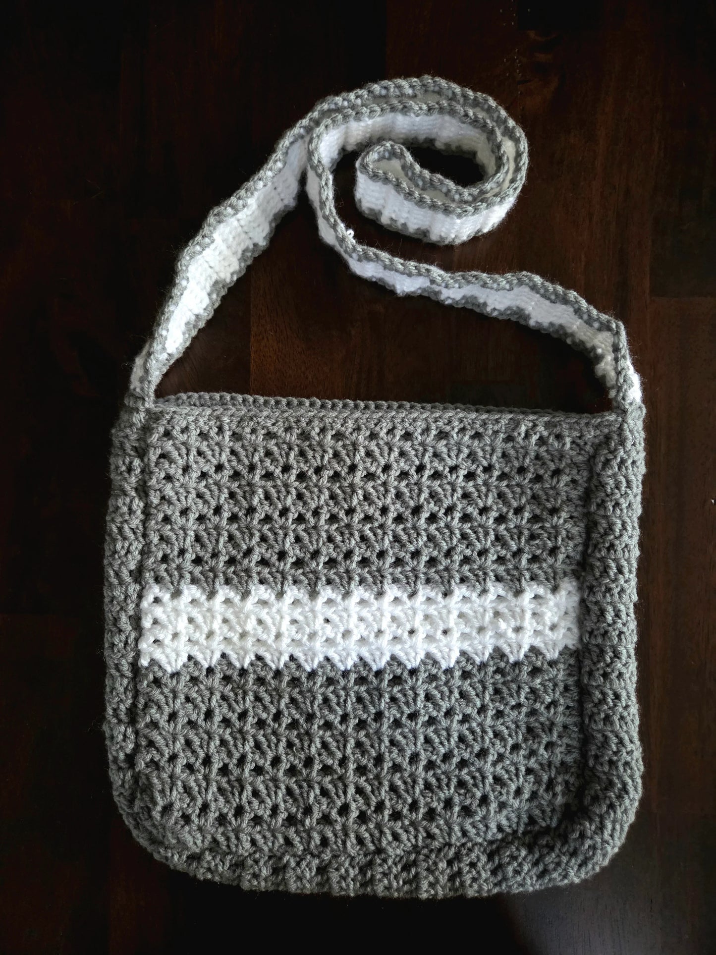 Handmade gray and white crochet shoulder bag on a dark wooden surface