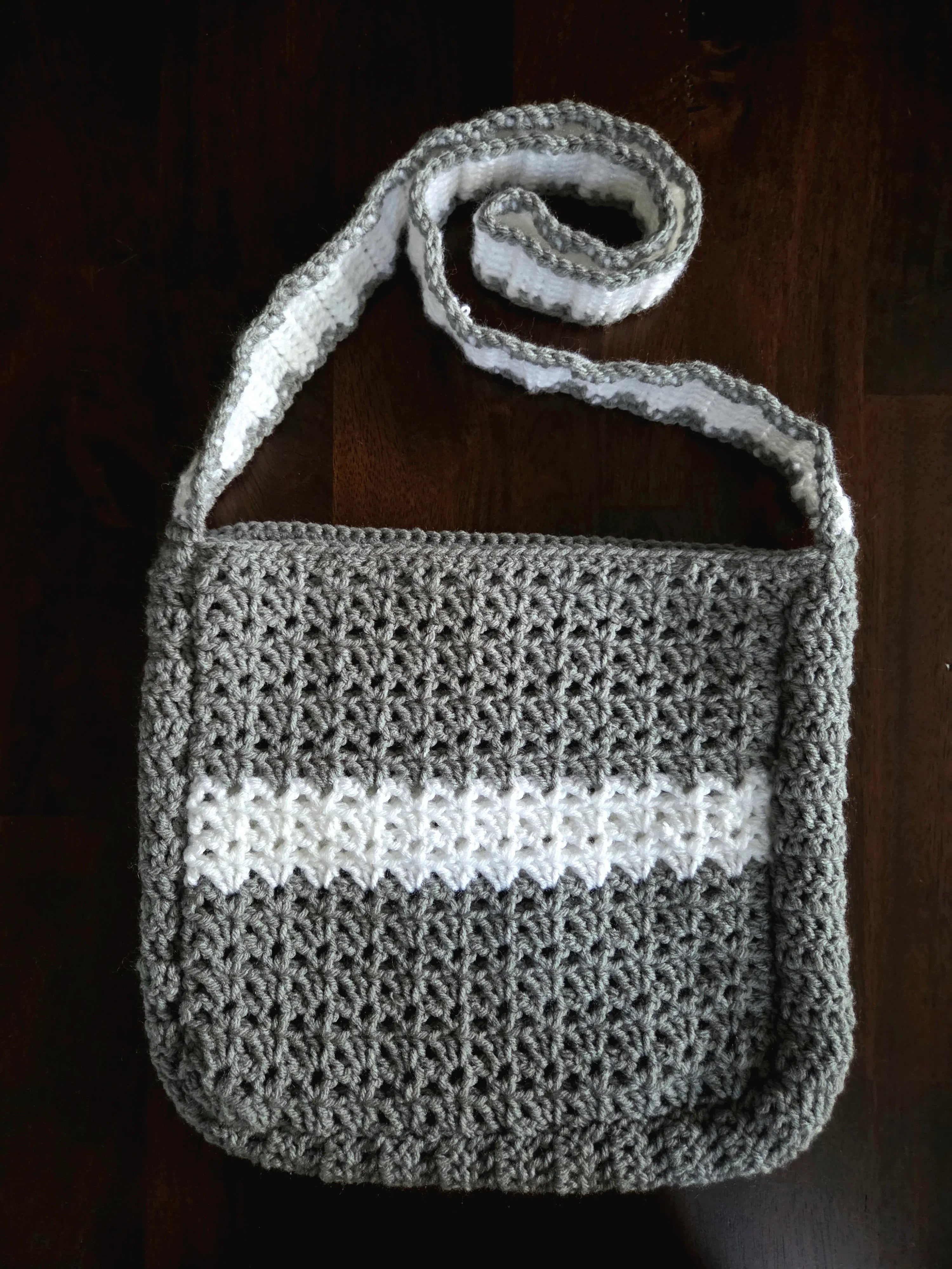 Handmade gray and white crochet shoulder bag on a dark wooden surface