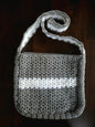 Handmade gray and white crochet shoulder bag on a dark wooden surface