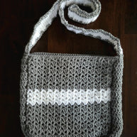 Handmade gray and white crochet shoulder bag on a dark wooden surface