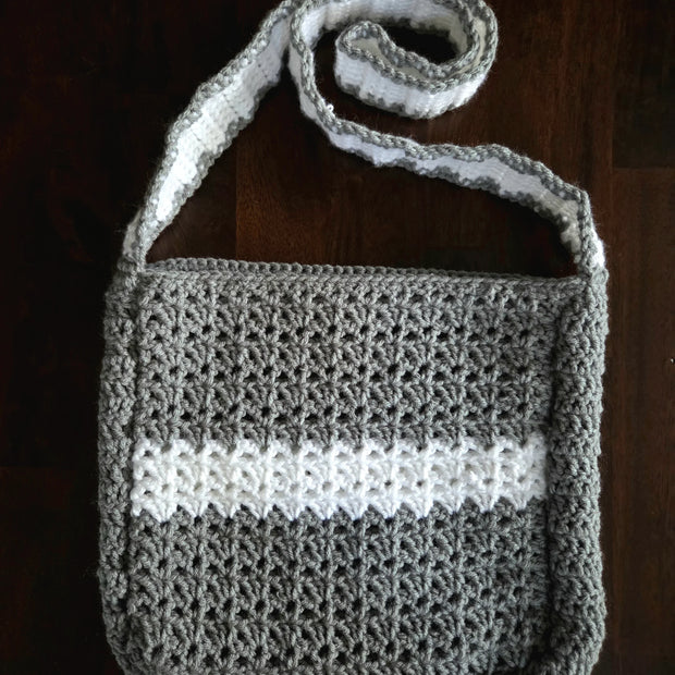 Handmade gray and white crochet shoulder bag on a dark wooden surface