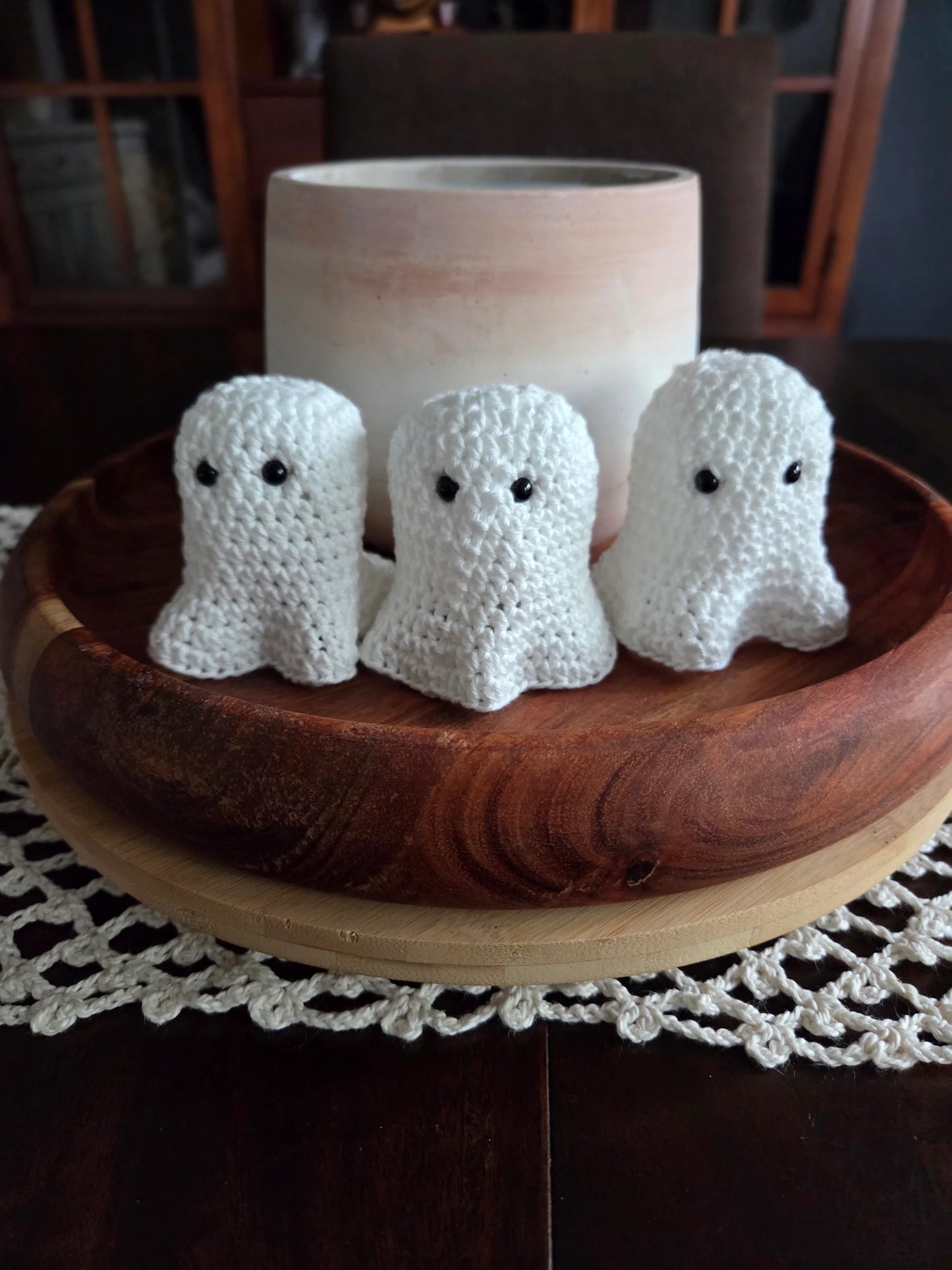 Three crocheted white ghost decorations in a wooden bowl on a lace doily table setting