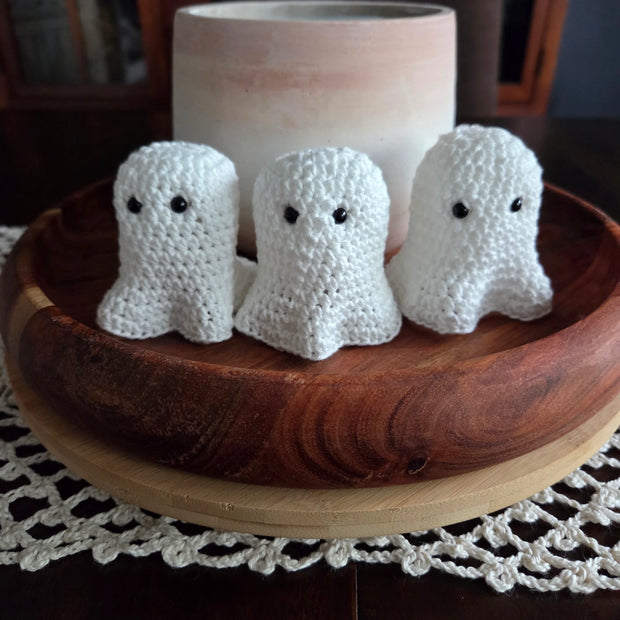 Three crocheted white ghost decorations in a wooden bowl on a lace doily table setting