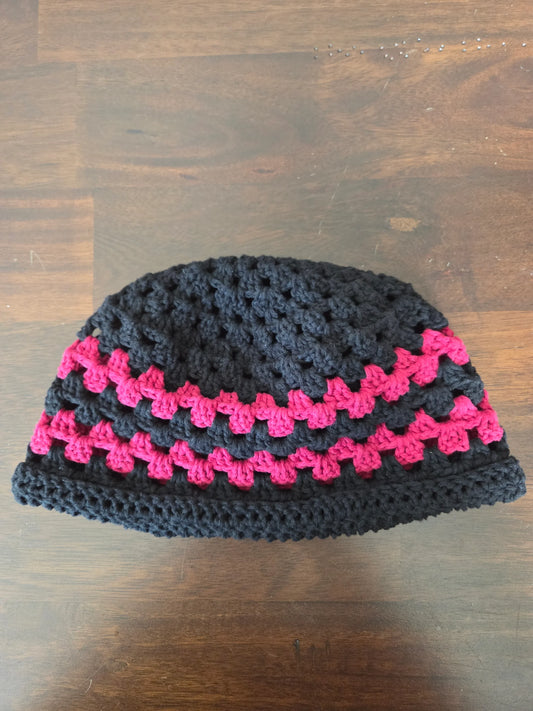 Handmade crochet beanie hat with black and pink yarn on a wooden table