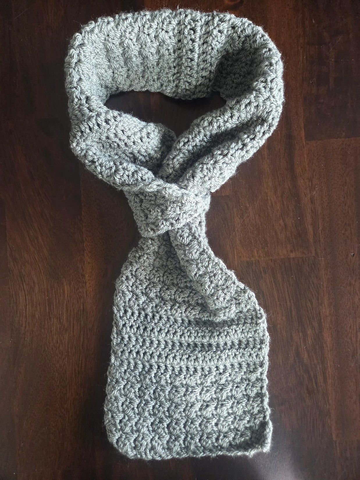 Handmade grey crochet scarf with textured pattern on dark wood table