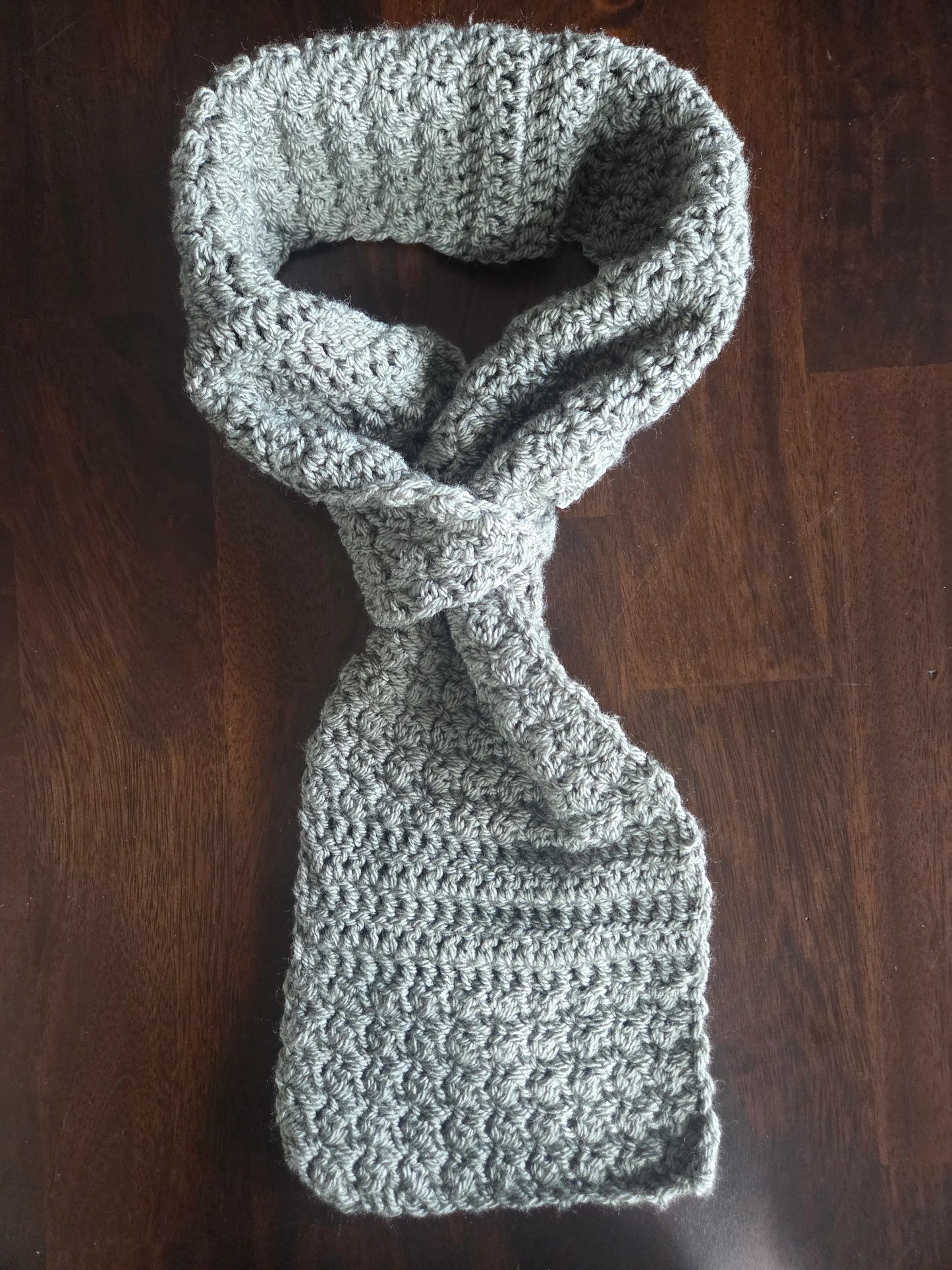 Handmade grey crochet scarf with textured pattern on dark wood table