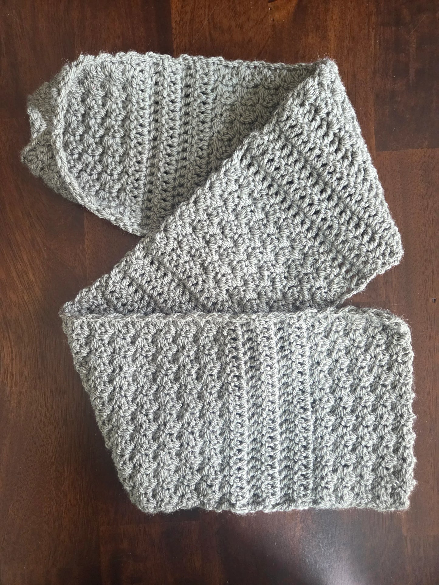 Gray crochet scarf with textured stitch detail on dark wood table