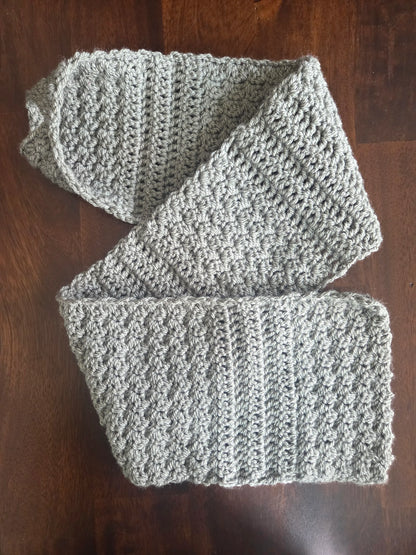 Gray crochet scarf with textured stitch detail on dark wood table
