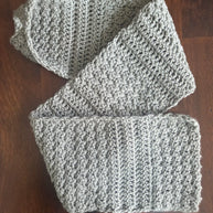 Gray crochet scarf with textured stitch detail on dark wood table