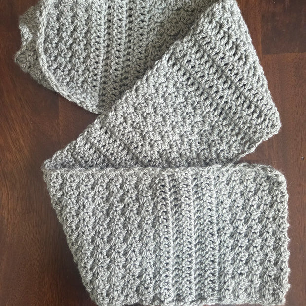Gray crochet scarf with textured stitch detail on dark wood table