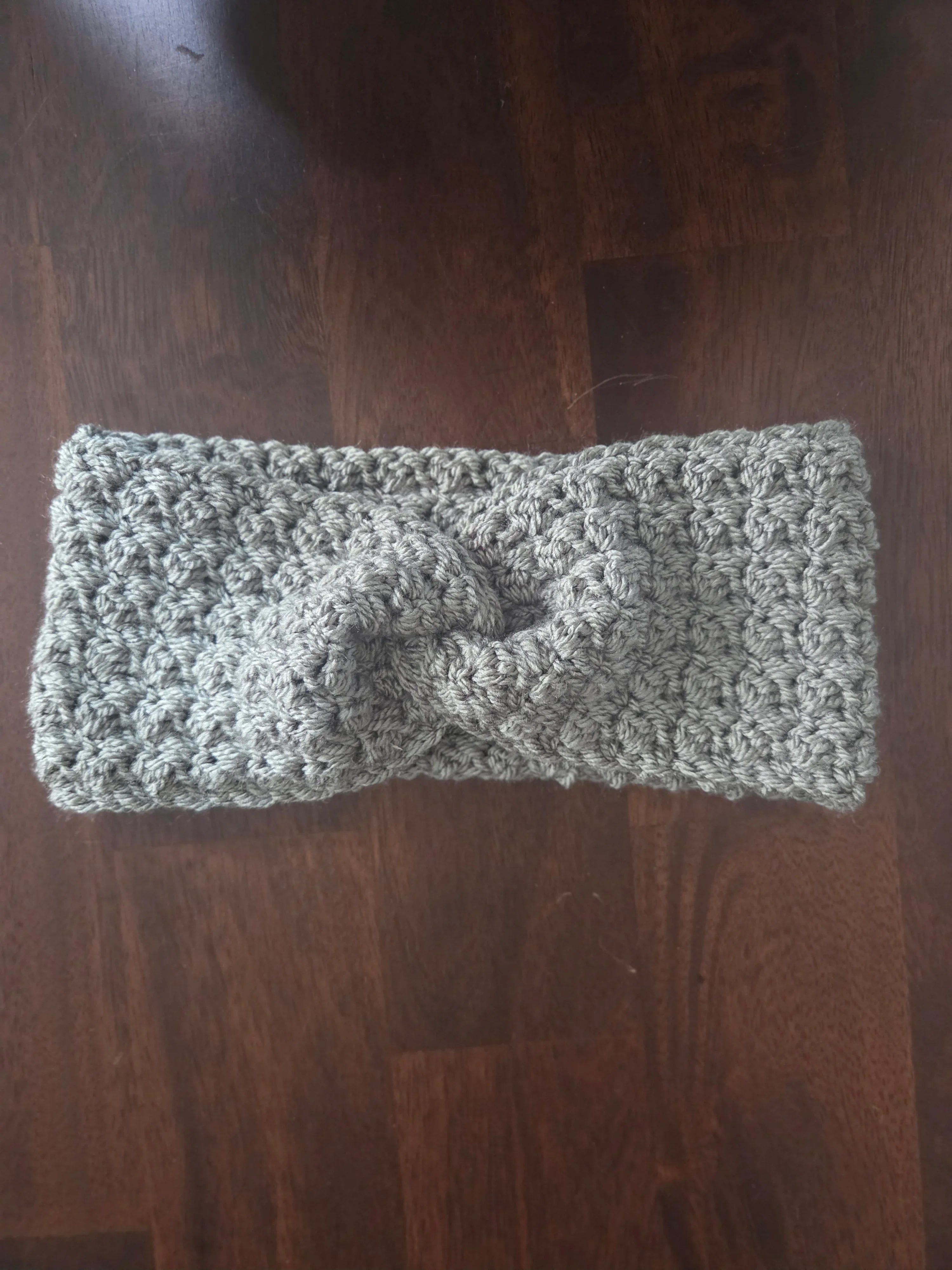 Gray chunky crochet headband with twist design on dark wooden table