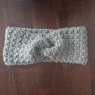 Gray chunky crochet headband with twist design on dark wooden table