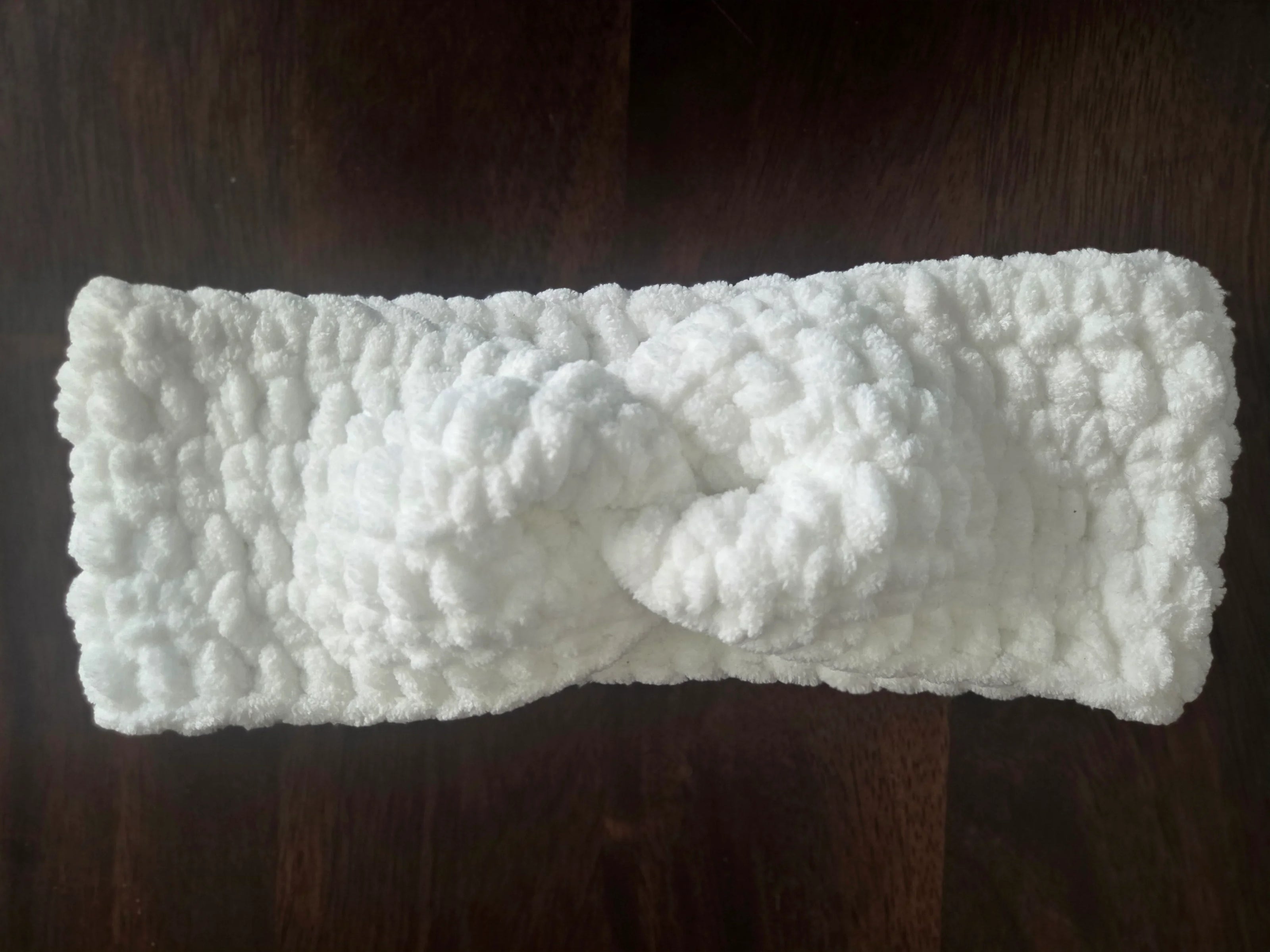 White crochet headband with knot detail on dark wooden surface