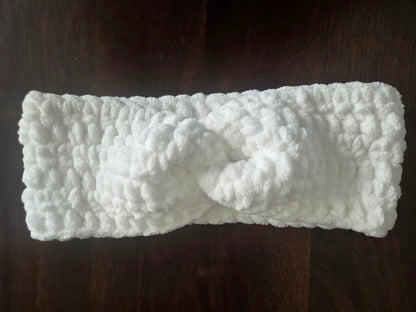 White crochet headband with knot detail on dark wooden surface