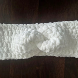 White crochet headband with knot detail on dark wooden surface