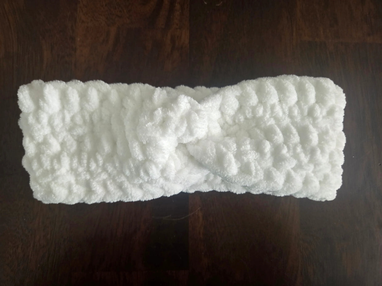 White fluffy knit headband with twist detail on dark wood surface