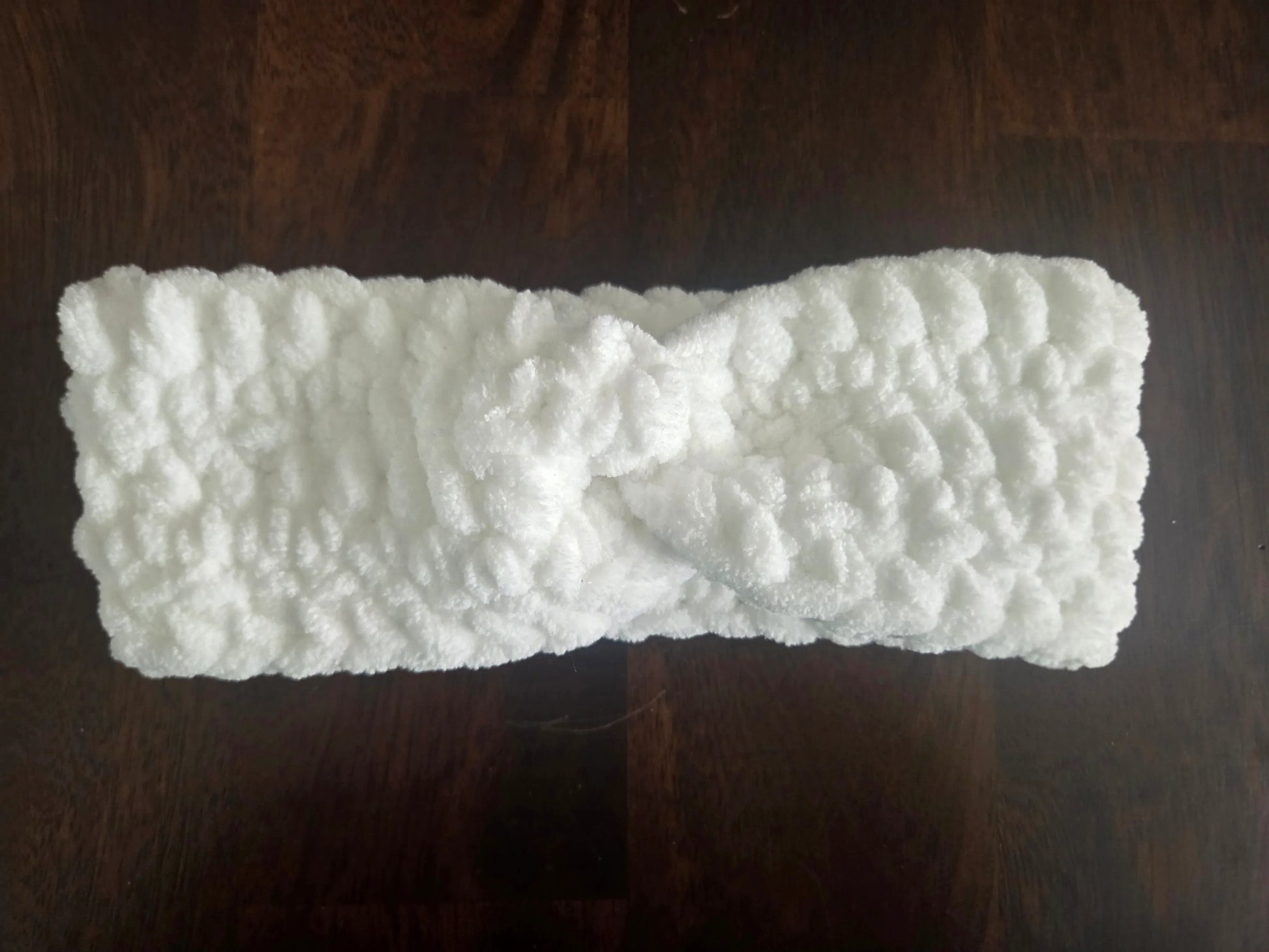 White fluffy knit headband with twist detail on dark wood surface