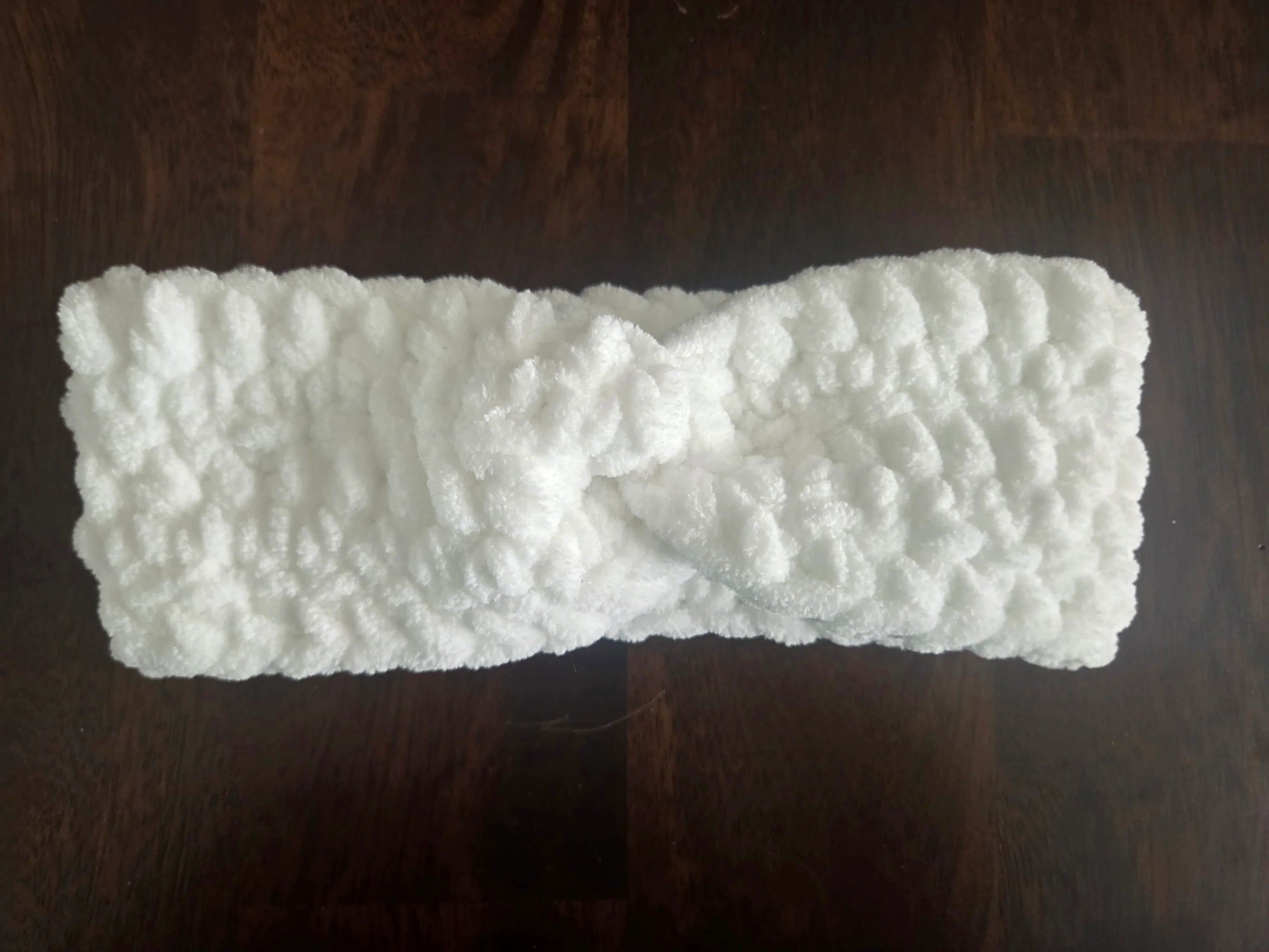 White fluffy knit headband with twist detail on dark wood surface