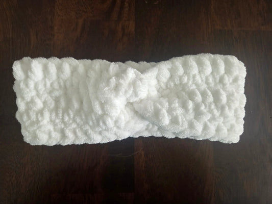 White fluffy knit headband with twist detail on dark wood surface