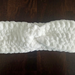 White fluffy knit headband with twist detail on dark wood surface