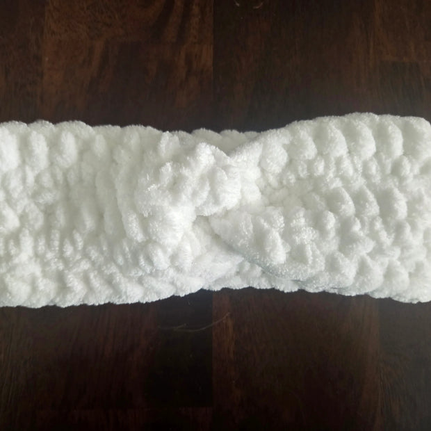 White fluffy knit headband with twist detail on dark wood surface