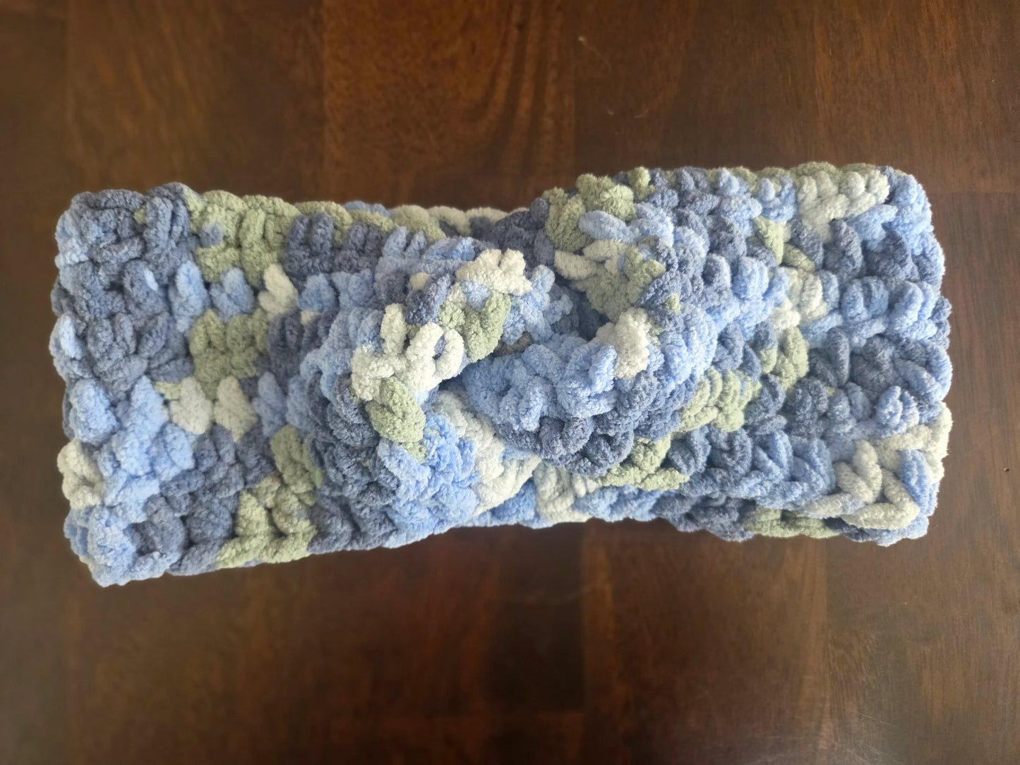 Chunky crocheted headband in blue, green, and white variegated yarn on wooden table