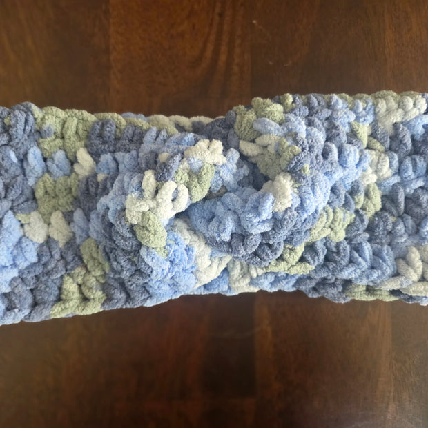 Chunky crocheted headband in blue, green, and white variegated yarn on wooden table