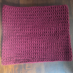 Handmade burgundy crochet cowl scarf on a wooden table