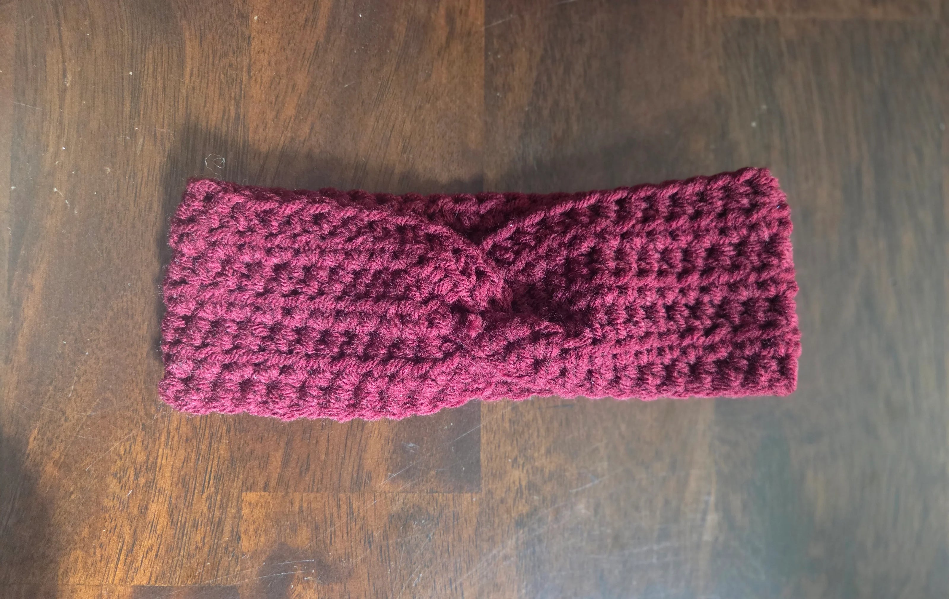 Handmade burgundy crochet headband with twisted knot on dark wood surface