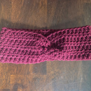 Handmade burgundy crochet headband with twisted knot on dark wood surface