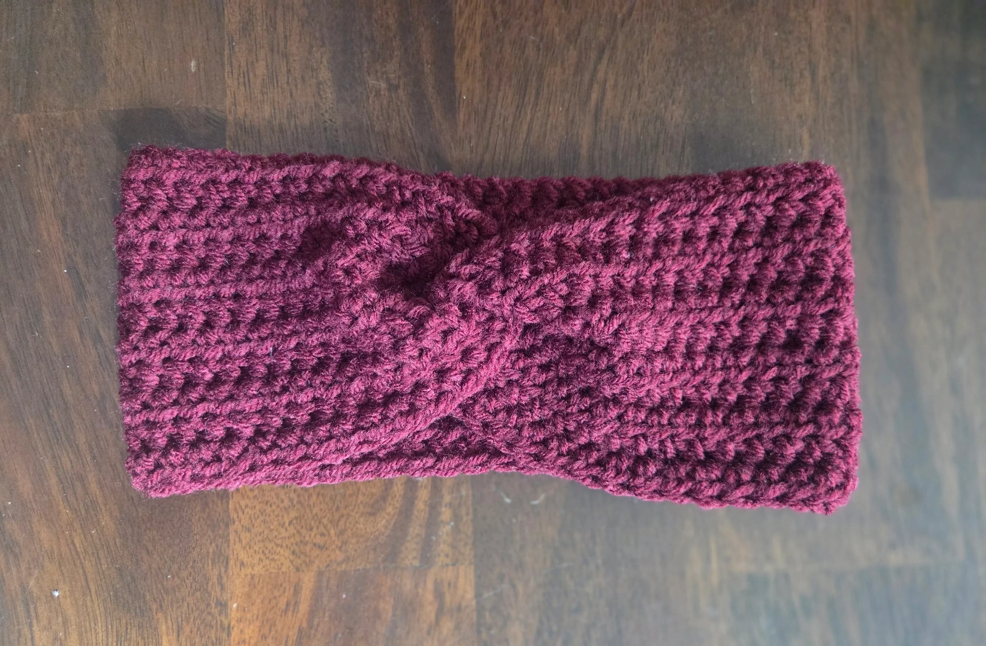 Handmade maroon crochet headband with twist detail on wood background