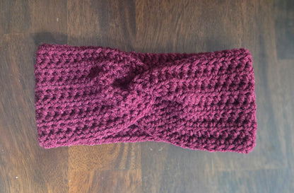 Handmade maroon crochet headband with twist detail on wood background