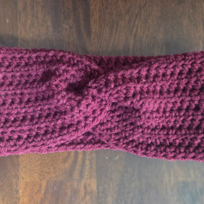 Handmade maroon crochet headband with twist detail on wood background