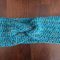 Handmade blue crochet headband with twist knot on wooden table