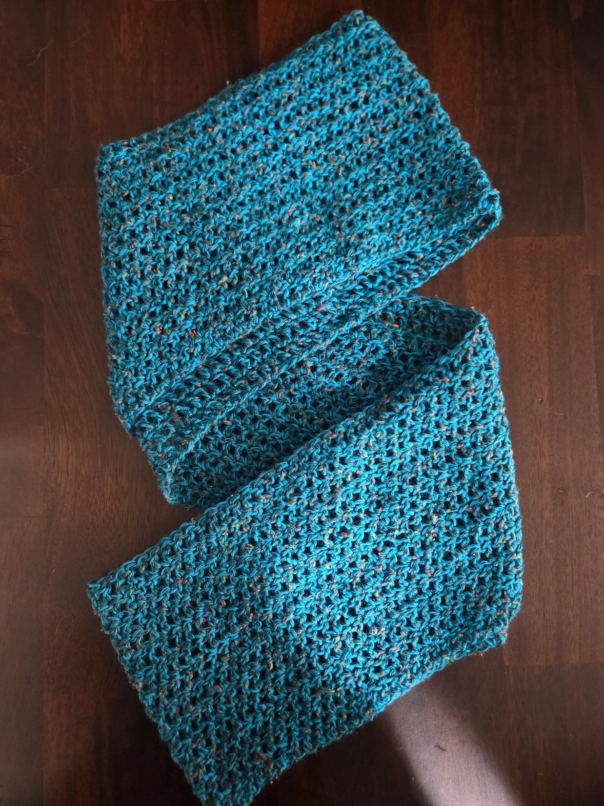 Handmade blue crochet scarf with textured pattern on dark wooden surface