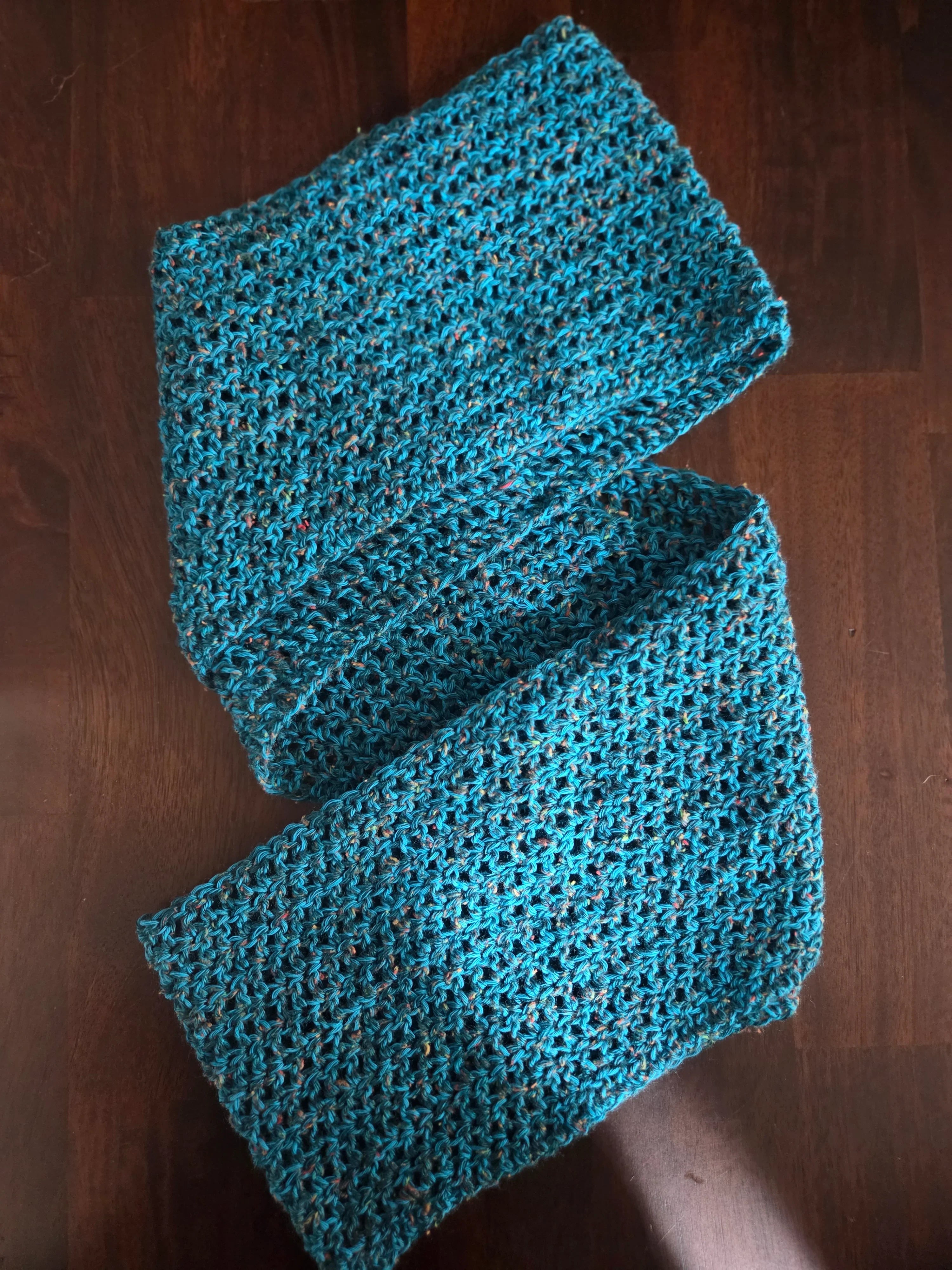 Handmade blue crochet scarf with textured pattern on dark wooden surface