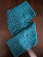 Handmade blue crochet scarf with textured pattern on dark wooden surface