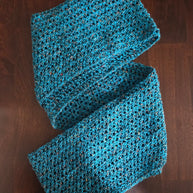 Handmade blue crochet scarf with textured pattern on dark wooden surface