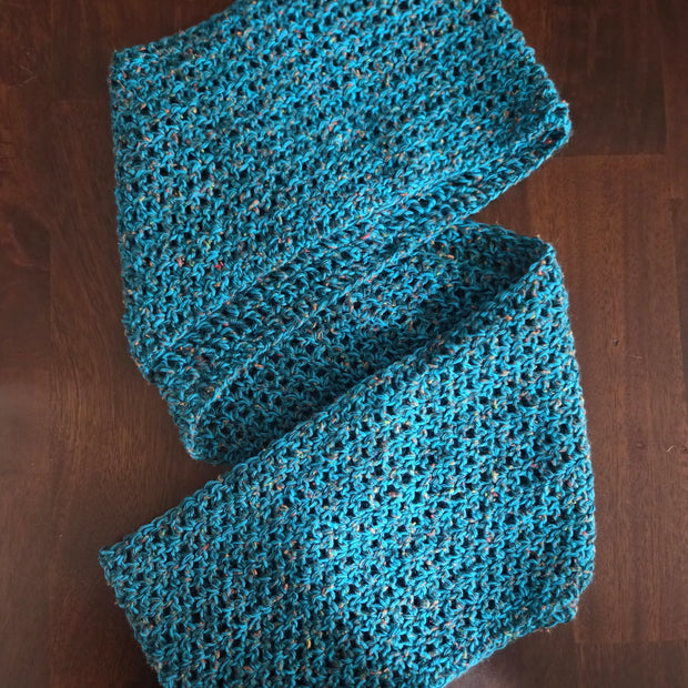 Handmade blue crochet scarf with textured pattern on dark wooden surface