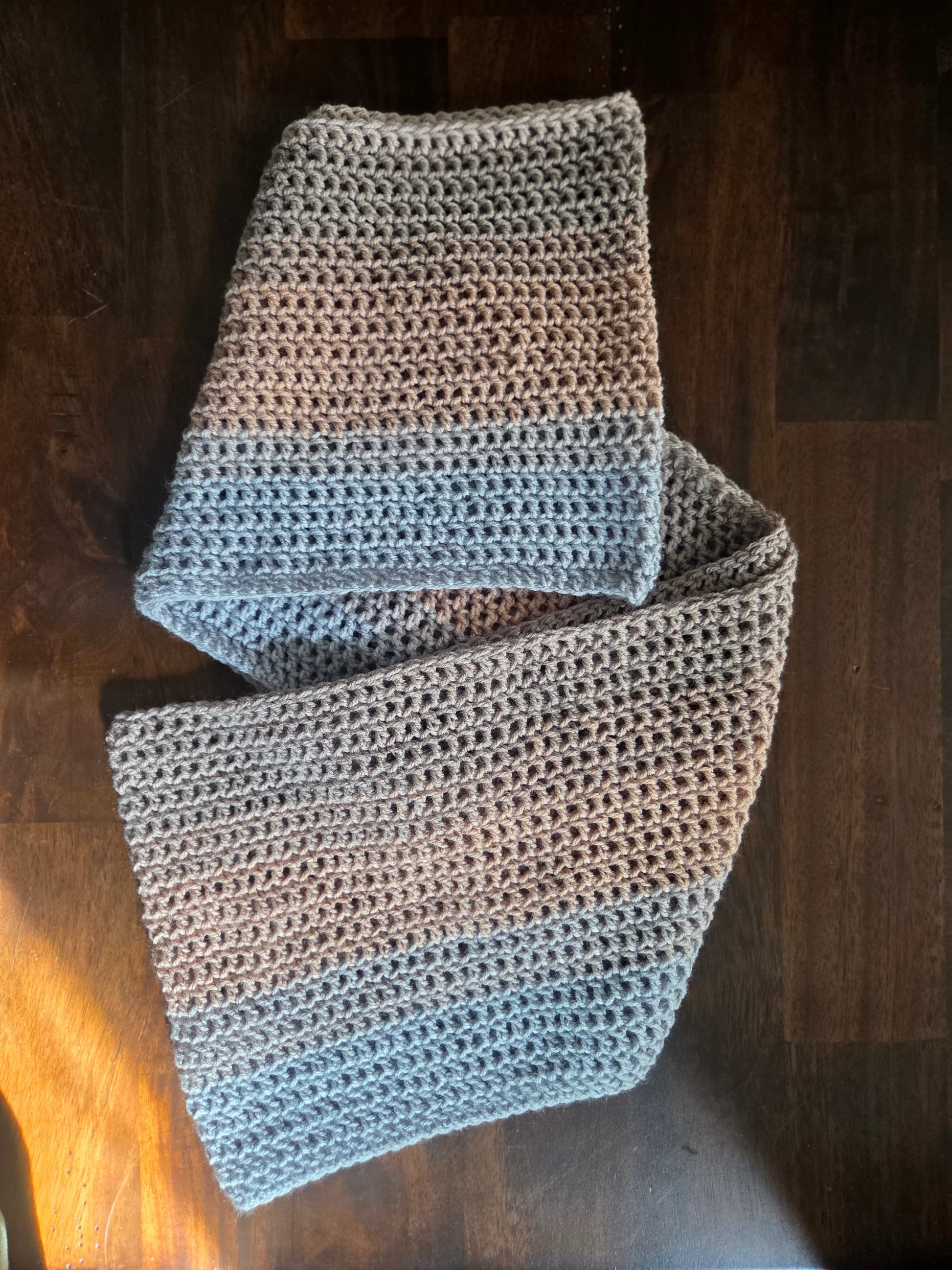 Handmade crochet scarf with grey and blue yarn on a dark wooden table