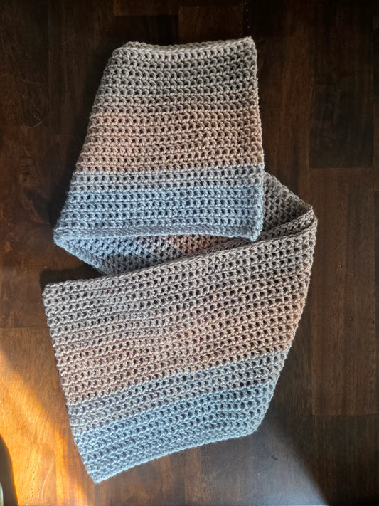 Handmade crochet scarf with grey and blue yarn on a dark wooden table