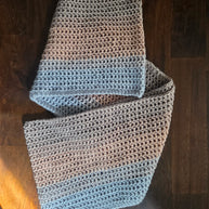Handmade crochet scarf with grey and blue yarn on a dark wooden table
