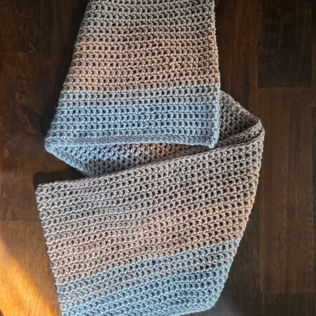 Handmade crochet scarf with grey and blue yarn on a dark wooden table