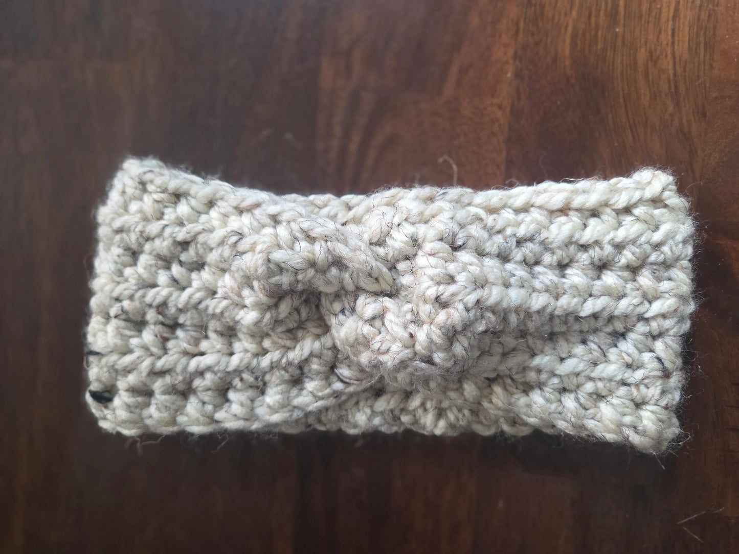 Handmade chunky knit beige headband with twist detail on wooden background
