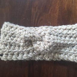 Handmade chunky knit beige headband with twist detail on wooden background