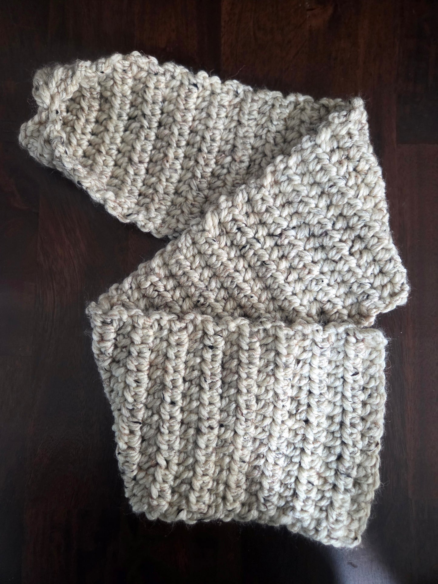 Handmade chunky beige knit scarf on dark wood table