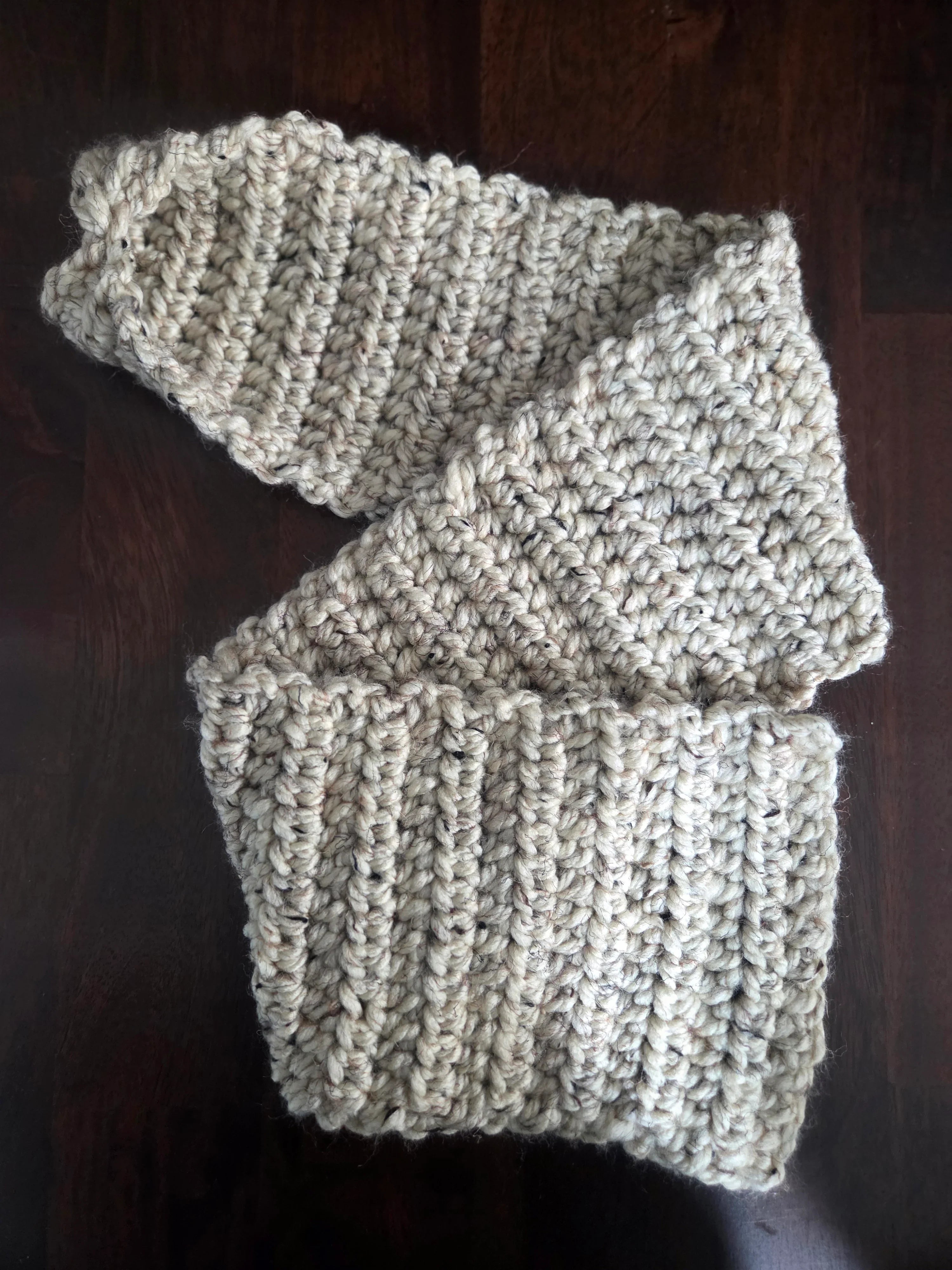 Handmade chunky beige knit scarf on dark wood table