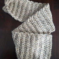 Handmade chunky beige knit scarf on dark wood table