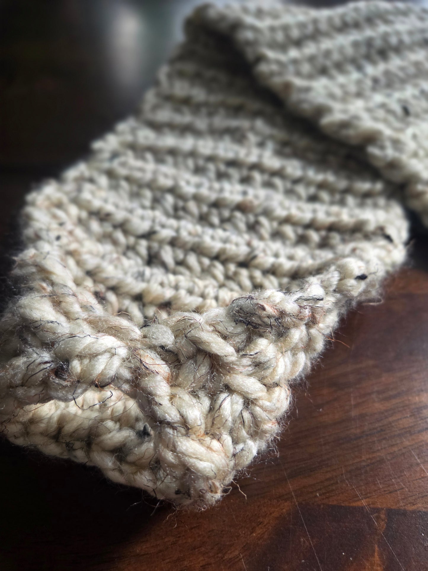 Chunky hand-knitted beige scarf with thick yarn on a wooden table