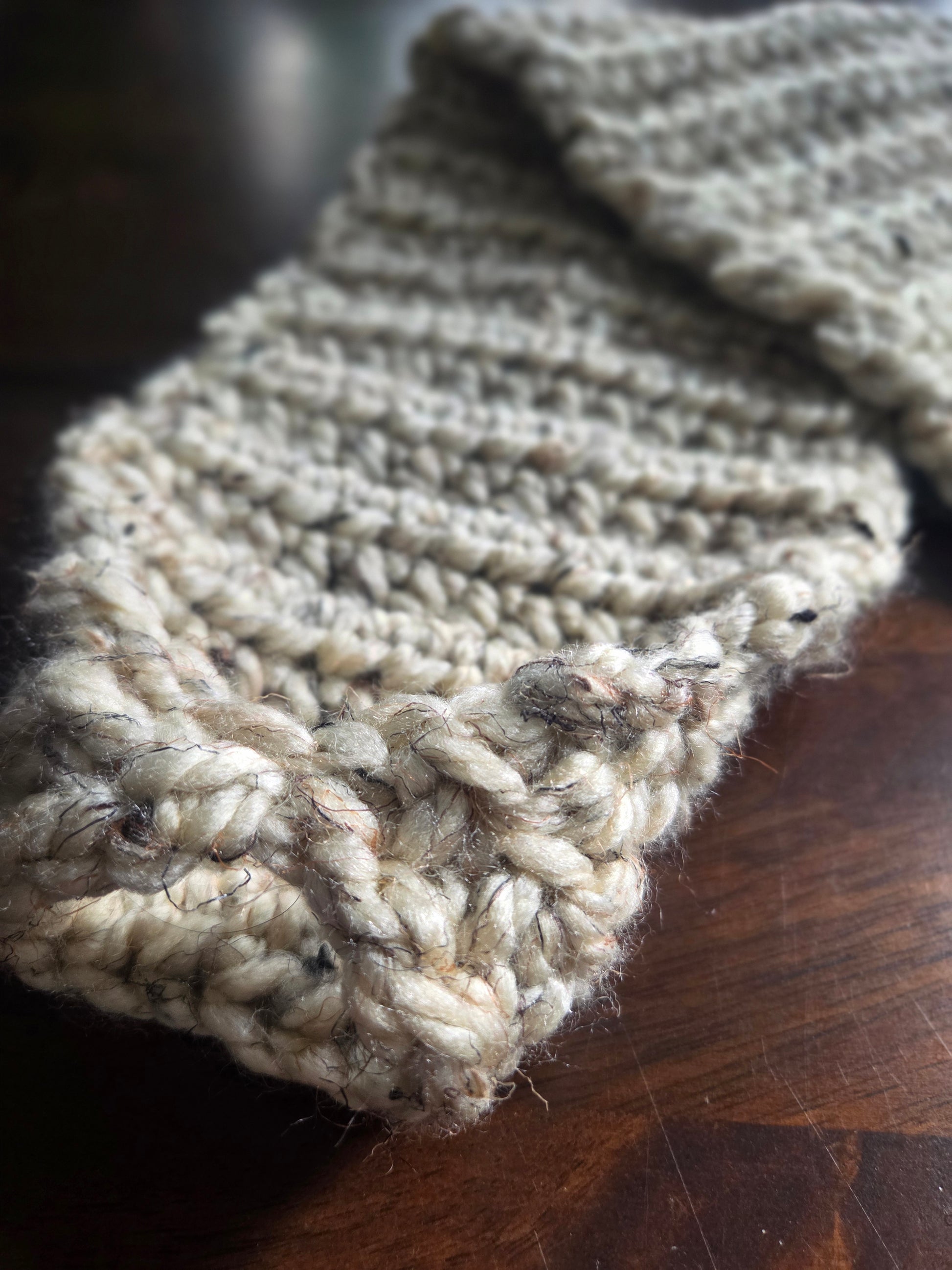 Chunky hand-knitted beige scarf with thick yarn on a wooden table